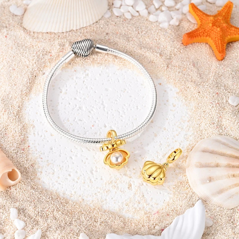 Gold-tone clamshell dangle charm with pearl on a bracelet and loose on sand with shells
