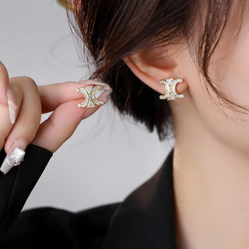 Gold-tone double crescent baguette stud worn on the earlobe while a matching stud is held near the ear