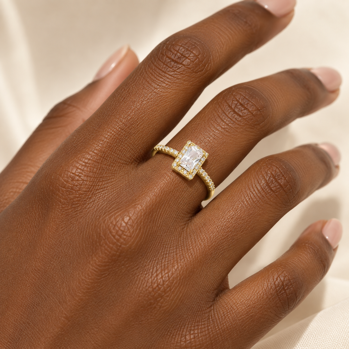 Deep brown skin hand wearing gold-tone square halo adjustable ring