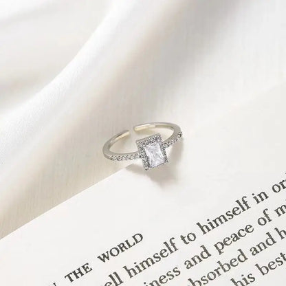 Silver-tone square halo adjustable ring with clear stone displayed on a book page