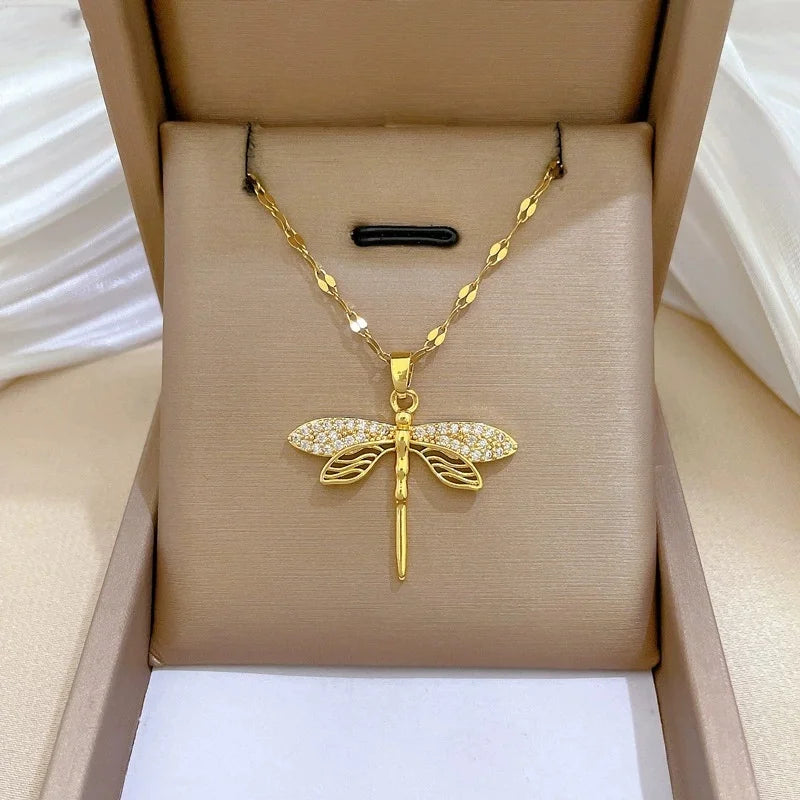 Gold-tone dragonfly pendant with pavé wings positioned on a beige jewelry box insert