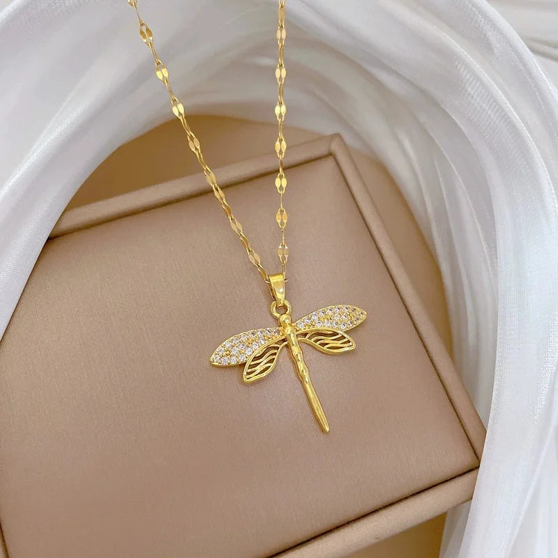 Gold-tone dragonfly pendant on a tan display with draped white fabric