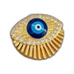 Gold-tone eye pendant with blue center and radiant fringe resting on a beige cushion