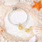 Gold-tone clamshell dangle charm with pearl on a bracelet and loose on sand with shells