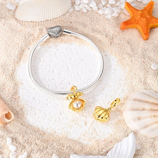 Gold-tone clamshell dangle charm with pearl on a bracelet and loose on sand with shells
