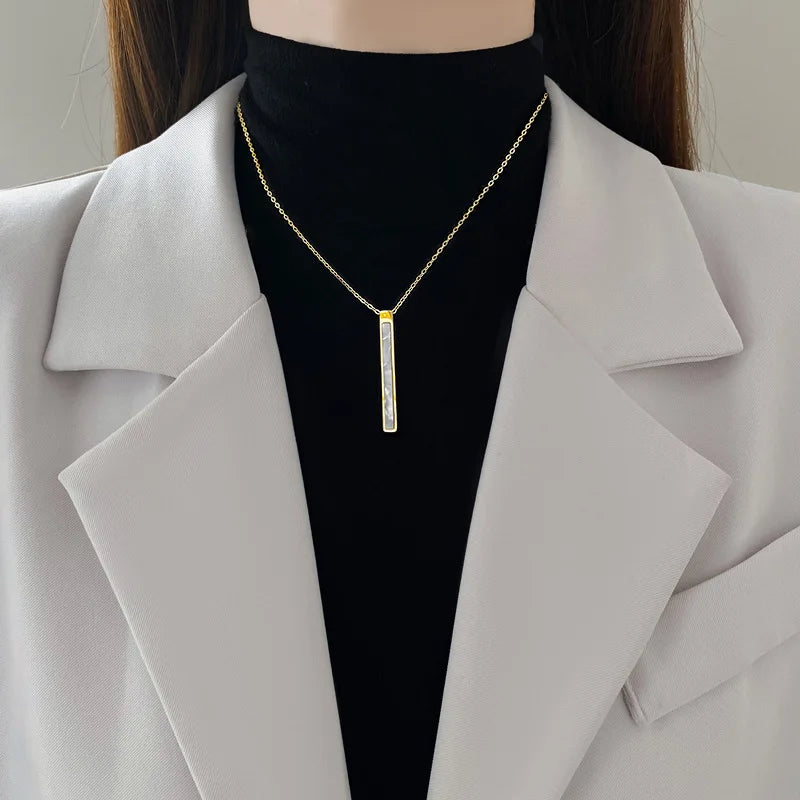 Gold-tone vertical bar pendant necklace worn at the collarbone