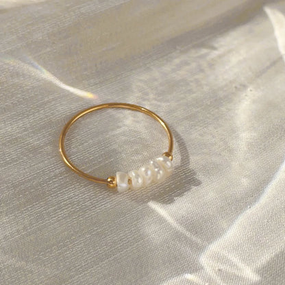 Gold-tone thin ring with irregular pearl beads on satin fabric in warm light