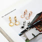 Gold-, rose-, and silver-tone Roman numeral hoop drop earrings with white or black inlays displayed on a magazine page