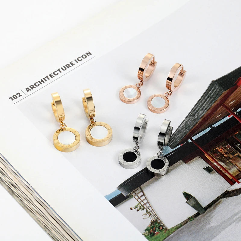Gold-, rose-, and silver-tone Roman numeral hoop drop earrings with white or black inlays displayed on a magazine page