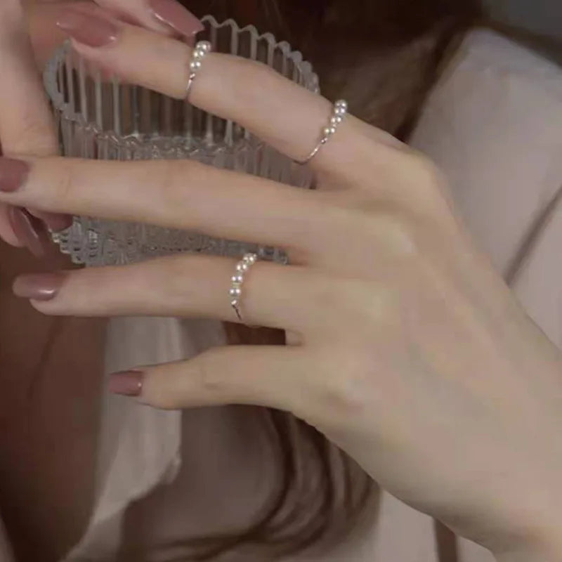 Gold-tone pearl stacking rings worn on fingers while holding a textured glass