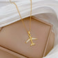 Gold-tone airplane pendant necklace resting on a beige display cushion with white drape