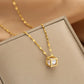 Gold-tone cube pendant necklace with inset clear stones resting on a fabric-lined jewelry box
