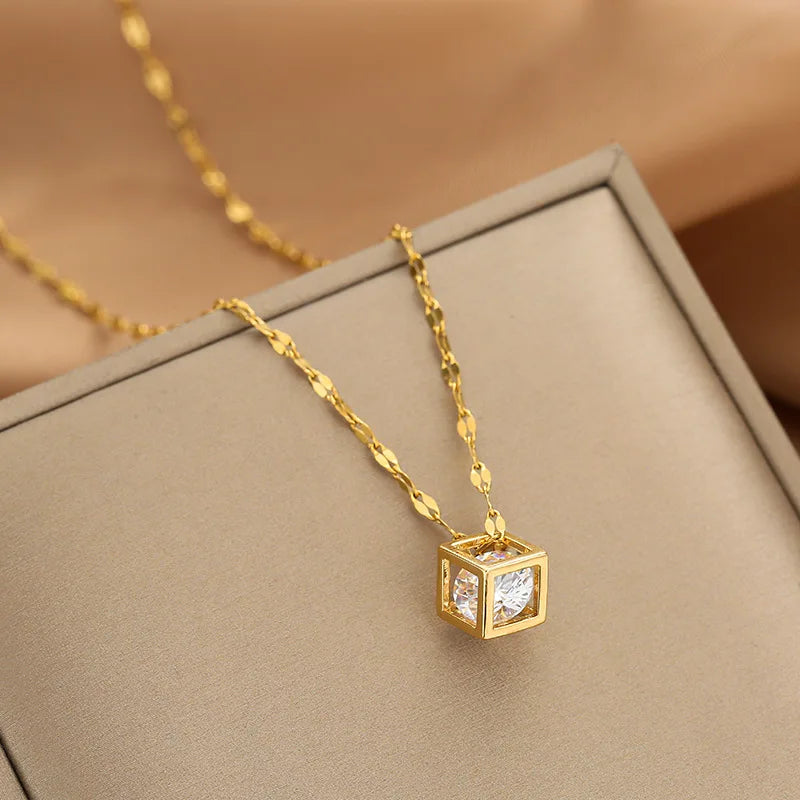 Gold-tone cube pendant necklace with inset clear stones resting on a fabric-lined jewelry box
