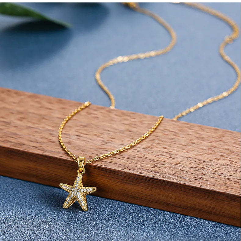 Gold-tone pavé starfish pendant resting at the edge of a wooden block against blue background