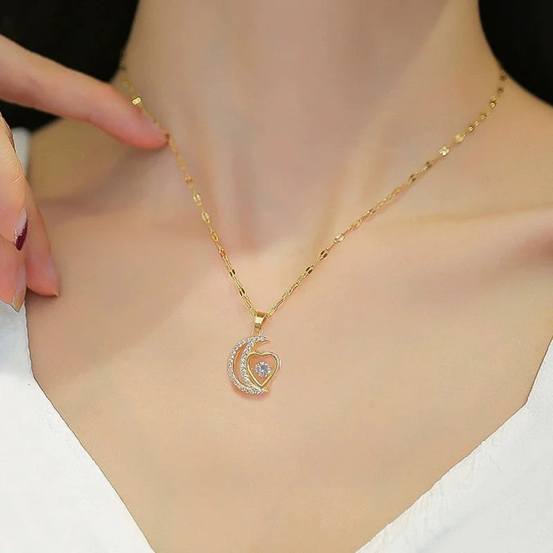 Gold-tone heart-and-moon pendant necklace worn at the collarbone with a finger nearby