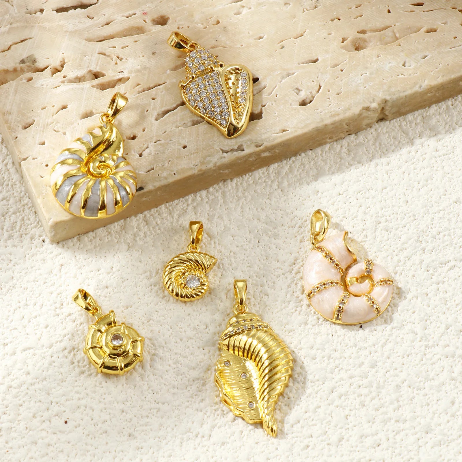 Flat-lay of six gold-tone seashell pendants on textured stone and fabric background