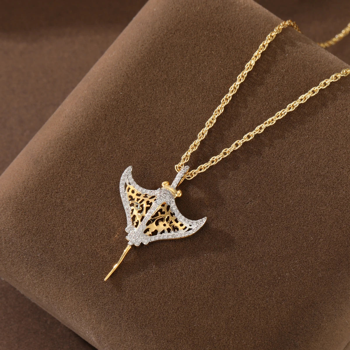 Two-tone manta ray pendant resting on brown suede display with twisted gold-tone chain