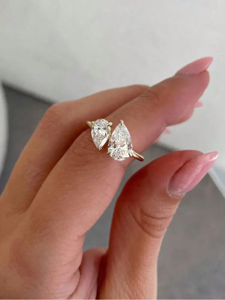 gold-tone bypass ring with two pear-cut stones held between fingertips
