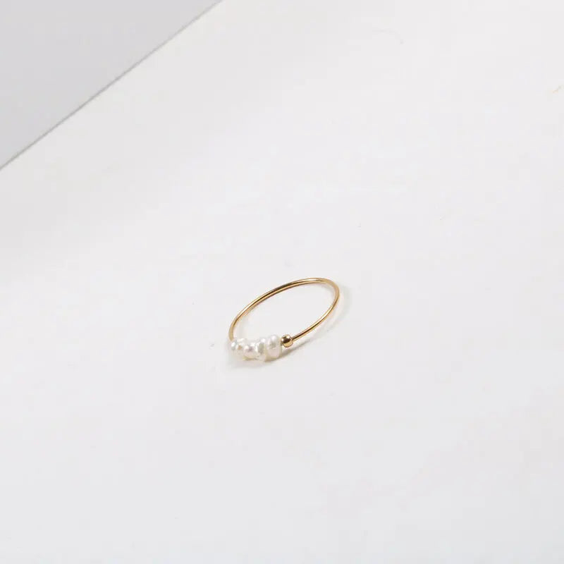 Delicate gold-tone thin ring featuring a row of irregular pearl beads on white