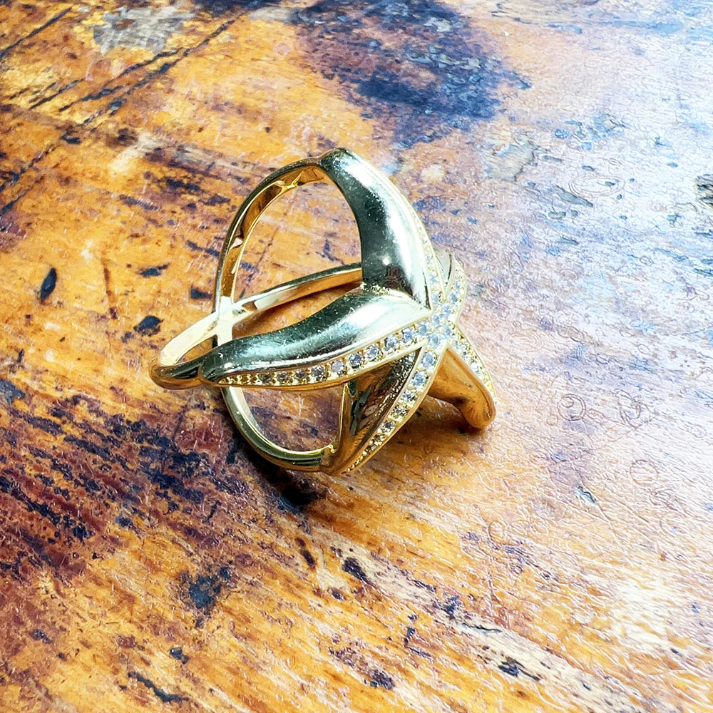 Gold-tone starfish pavé openwork ring angled on a wood surface showing side profile