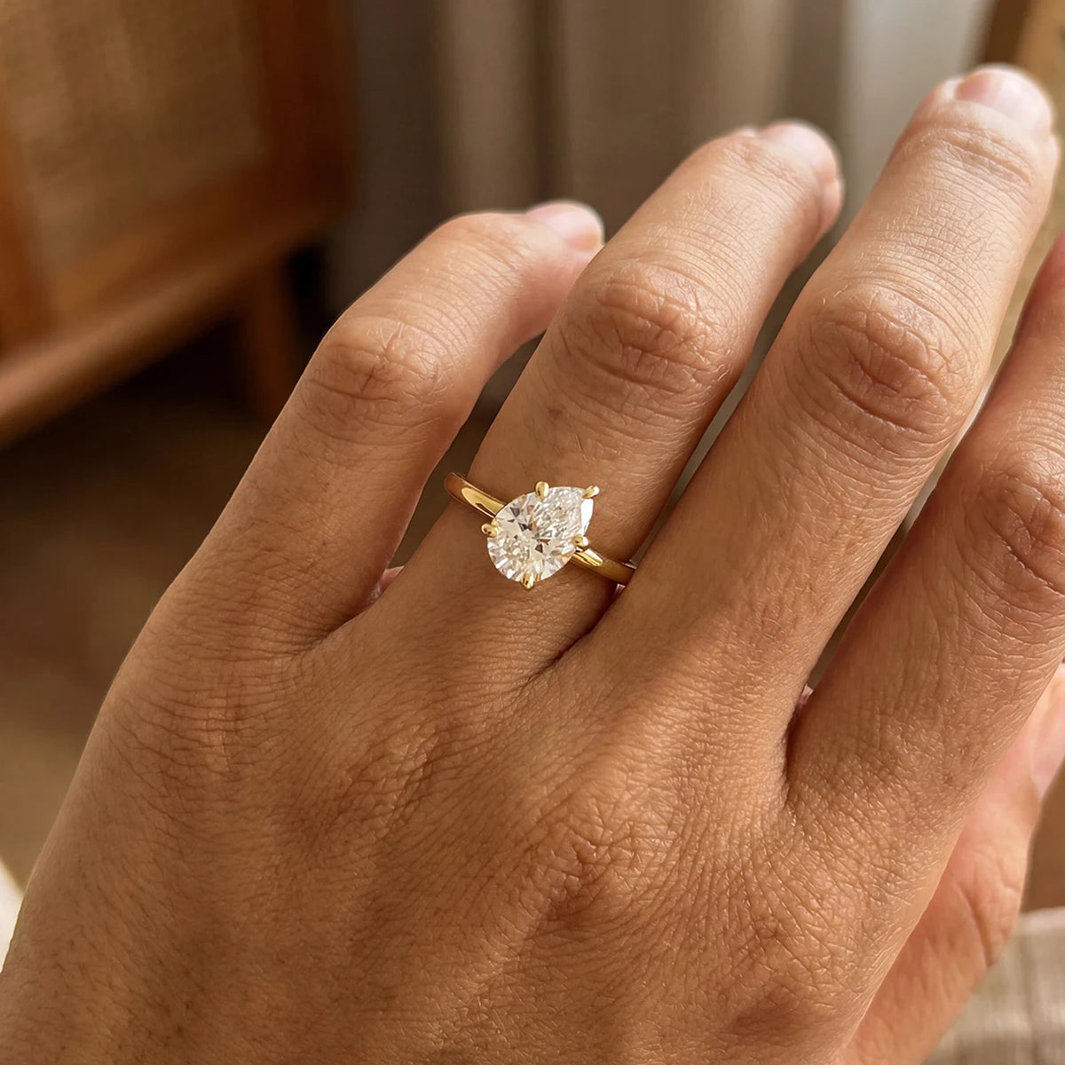 gold-tone pear-cut solitaire ring worn on the ring finger against a neutral background