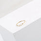 Gold-tone thin ring with irregular pearl beads sitting on the corner of a white block