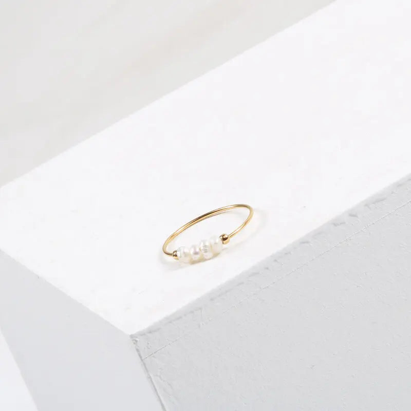 Gold-tone thin ring with irregular pearl beads sitting on the corner of a white block