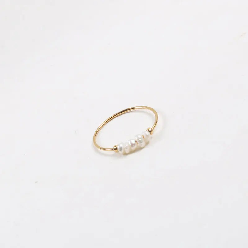 Simple gold-tone stacking ring with irregular pearl beads displayed on a white surface