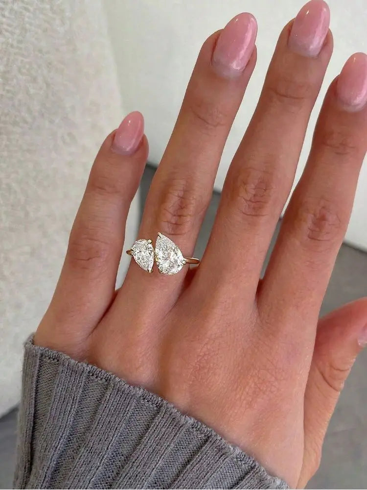 hand wearing a gold-tone bypass ring with two pear-cut stones on the ring finger