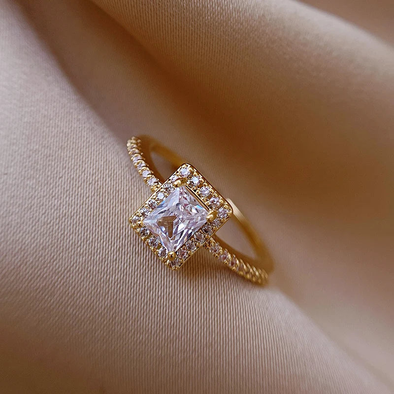 Gold-tone square halo adjustable open ring with clear center stone on champagne satin