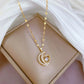 Crescent-and-heart gold-tone pendant necklace laid on a beige cushion beside white fabric