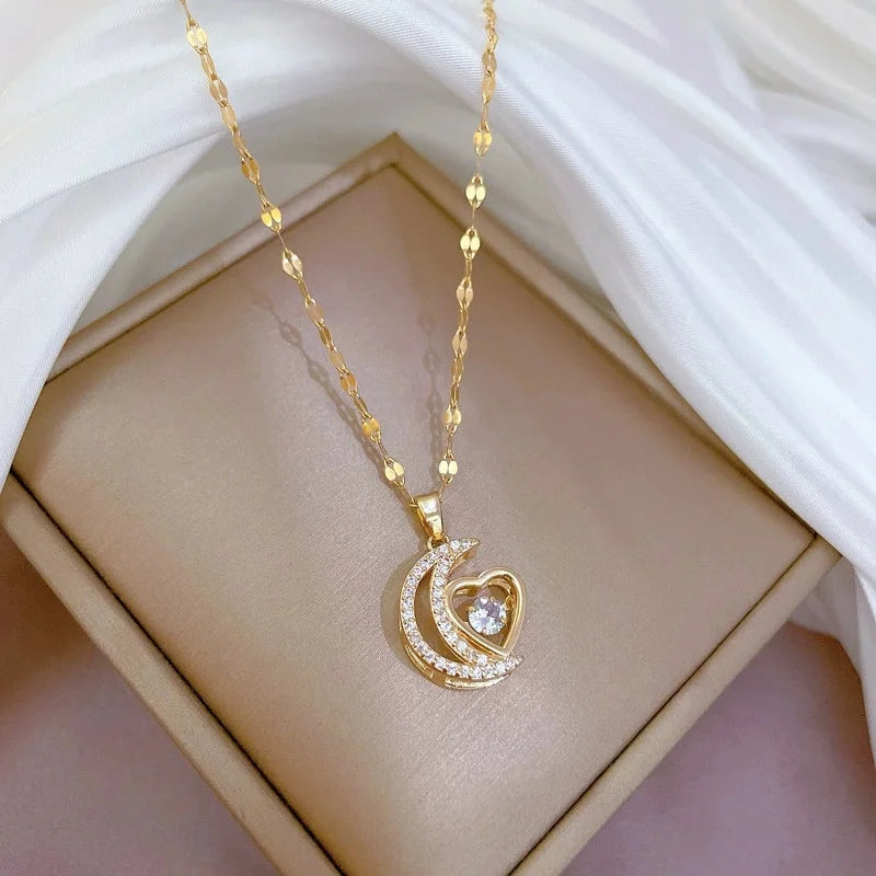 Crescent-and-heart gold-tone pendant necklace laid on a beige cushion beside white fabric