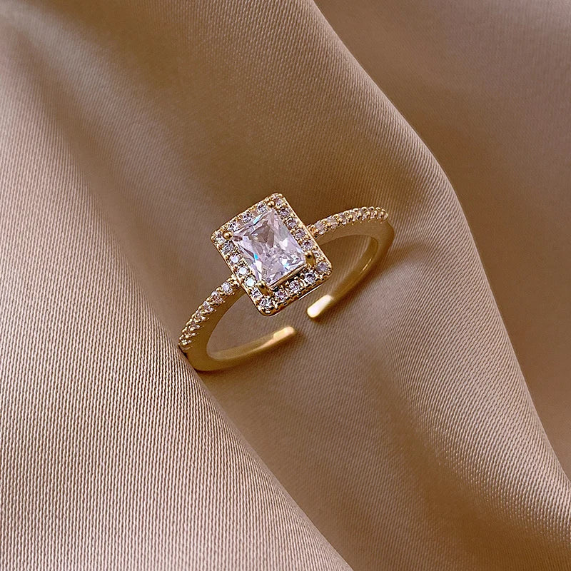 Gold-tone square halo open ring displayed on draped beige satin fabric