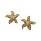 Gold-tone starfish stud earrings with pearl centers on a scalloped white dish