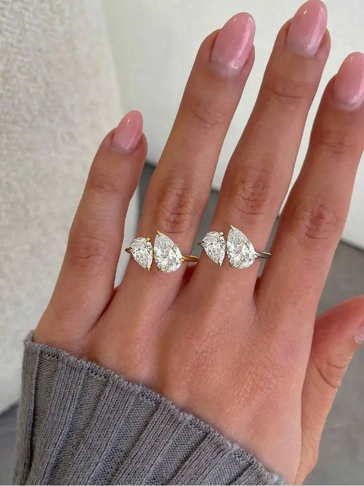 hand wearing gold-tone and silver-tone bypass rings with pear-cut stones on adjacent fingers