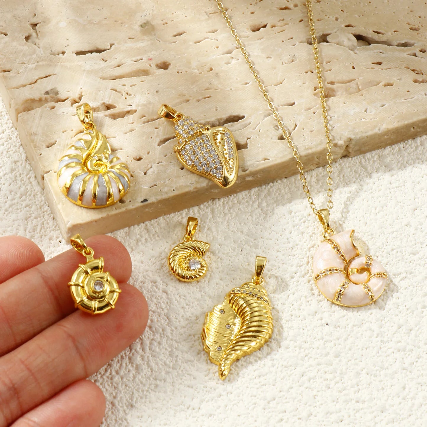 Gold-tone shell charms styled on stone with one pendant held between fingers for scale