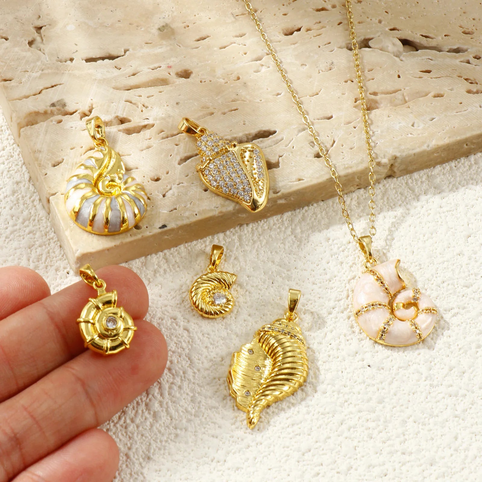 Gold-tone shell charms styled on stone with one pendant held between fingers for scale