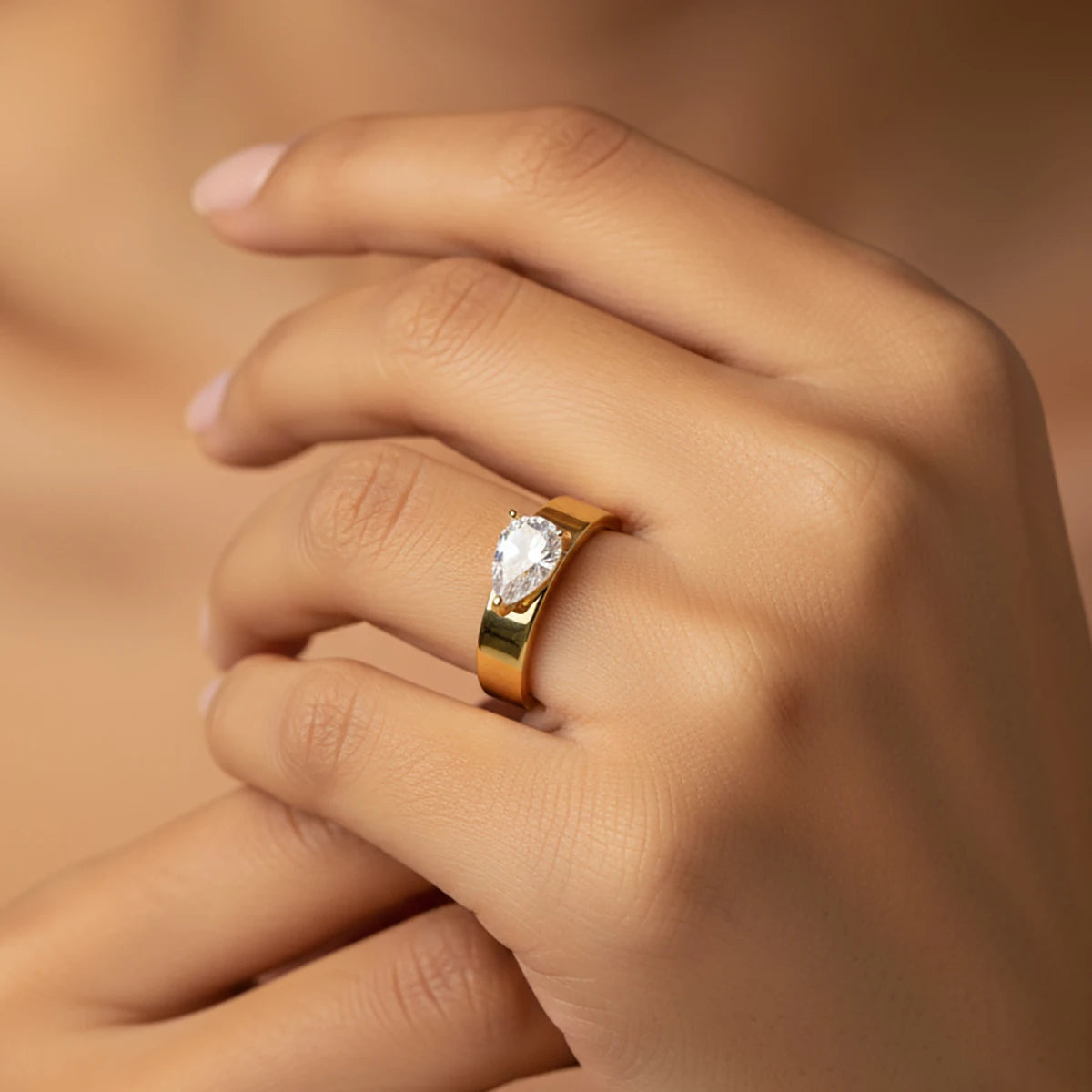 gold-tone ring with a single pear-cut stone worn on the finger
