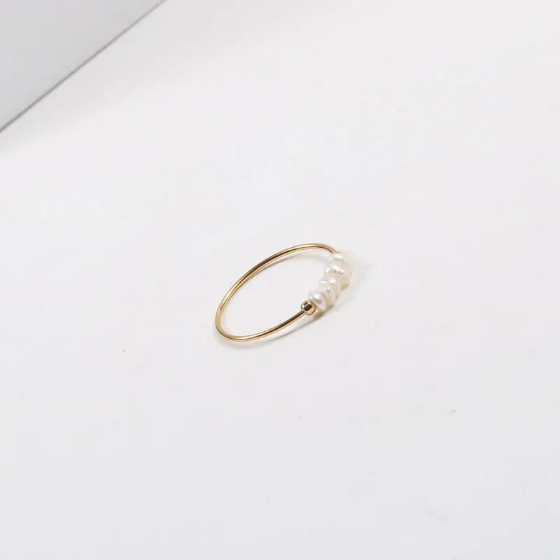 Gold-tone thin stacking ring with irregular pearl beads photographed at an angle