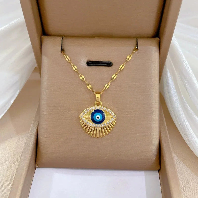 Gold-tone evil-eye pendant with blue center and fringe shown on a beige box insert