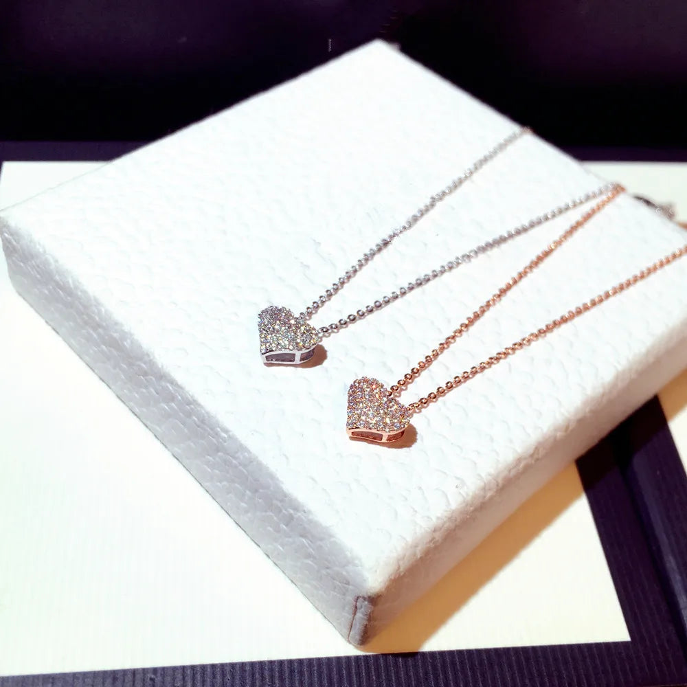 Two pavé heart necklaces displayed on a white textured box, one silver-tone and one rose gold-tone