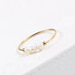 Gold-tone bead ring with a cluster of five pearly white beads, photographed at an angle on a light surface.