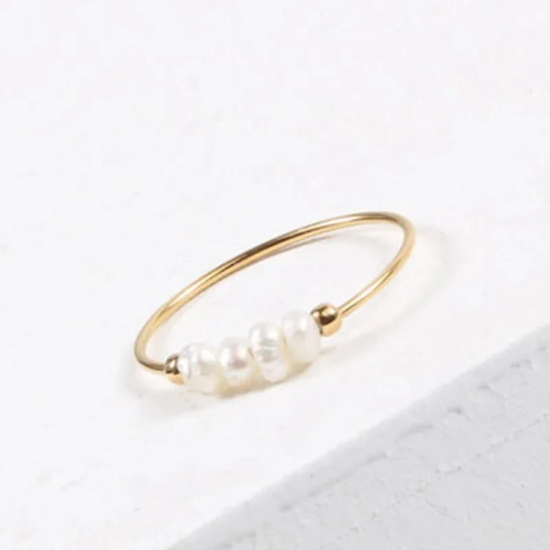 Gold-tone bead ring with a cluster of five pearly white beads, photographed at an angle on a light surface.