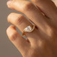 gold-tone bypass ring with a round center stone and pavé accents worn on the finger