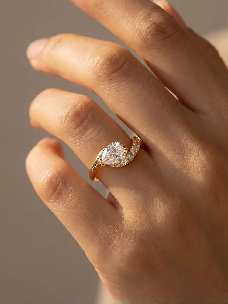 gold-tone bypass ring with a round center stone and pavé accents worn on the finger
