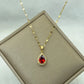 Gold-tone teardrop pendant necklace with red center resting on a cushioned display box