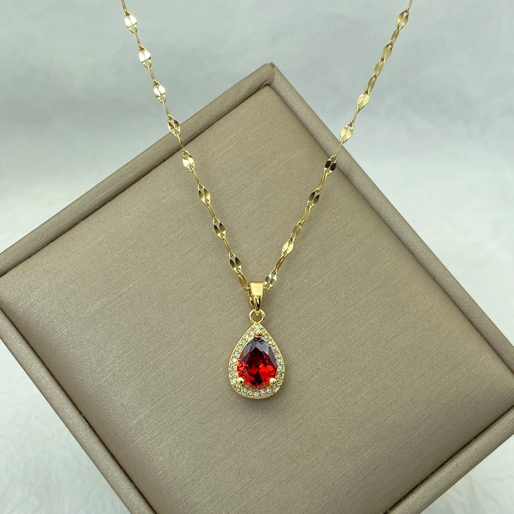 Gold-tone teardrop pendant necklace with red center resting on a cushioned display box