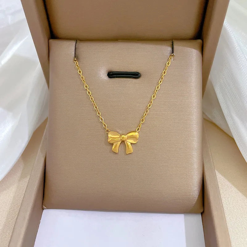 5b2a5e06-8155-44eb-9959-6322b5124a2d gold-tone bow pendant necklace on a beige display cushion