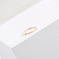 Minimal gold-tone stacking ring with irregular pearl beads on a white textured block