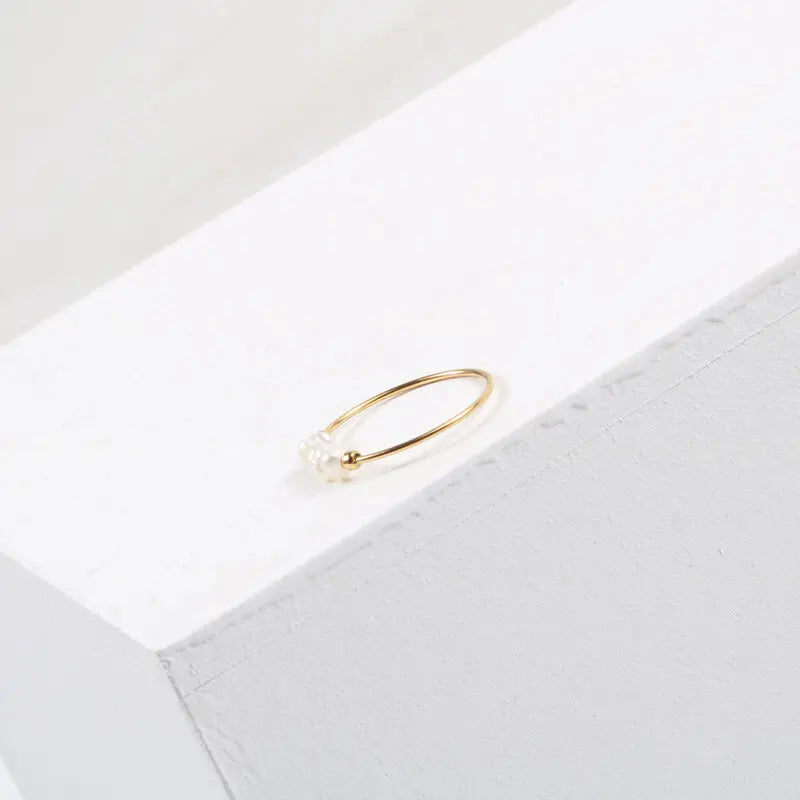 Minimal gold-tone stacking ring with irregular pearl beads on a white textured block